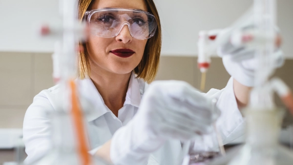 ​​Young female student sits in front of a microscope and enters data into a computer with the help of her female teacher.​ 